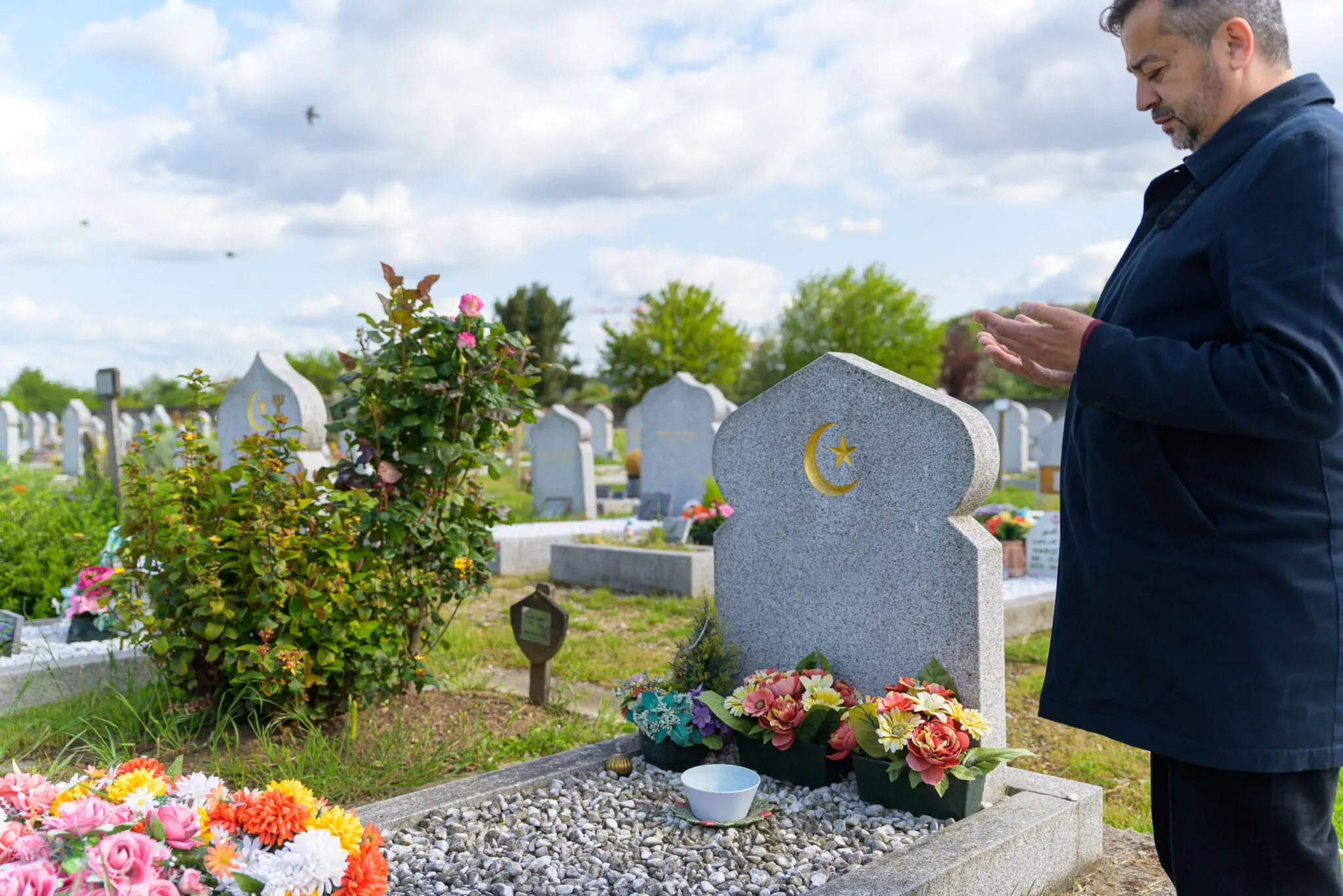 Homme en prière de recueillement devant une tombe musulmane ornée d'un croissant doré